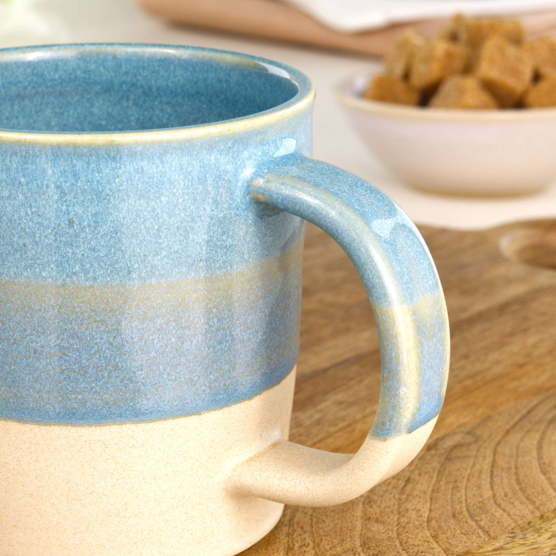 Close-up of the handle and layered Coastal Blue glaze over a sandy satin-matte base on a handmade ceramic mug from my home studio