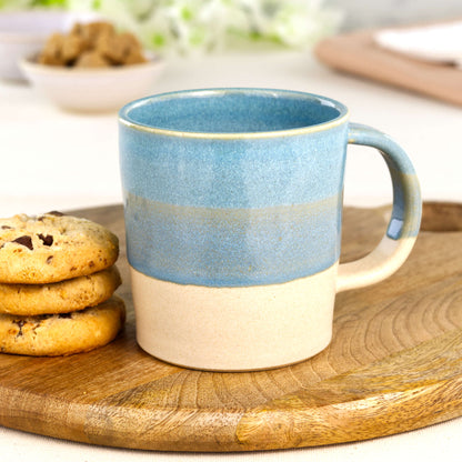 Coastal Blue and Sand artisan pottery mug on a wooden board with cookies, a wheel-thrown everyday mug made in my small UK studio
