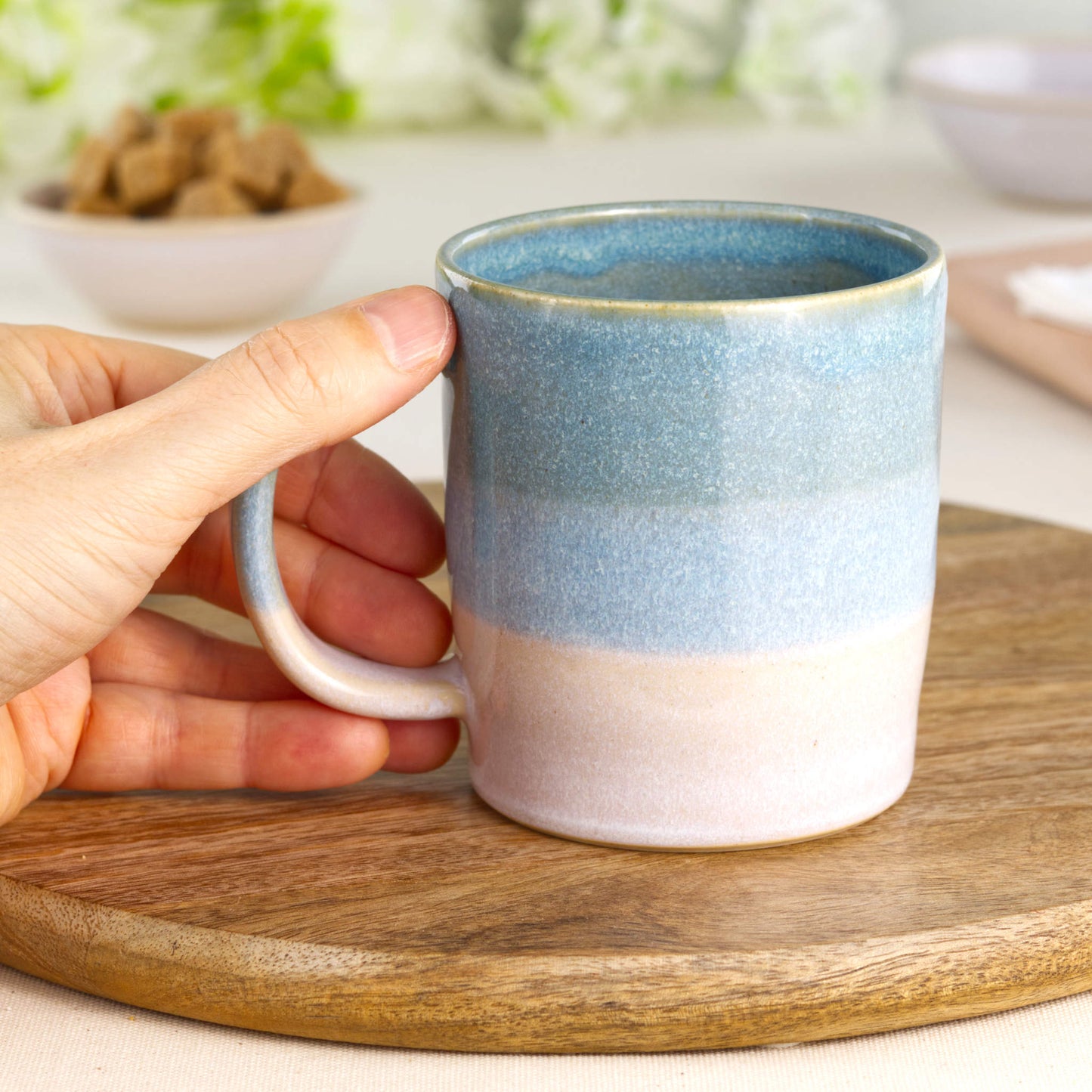 Wheel-thrown stoneware mug held in hand, showing comfortable handle and two-tone blue and white glaze