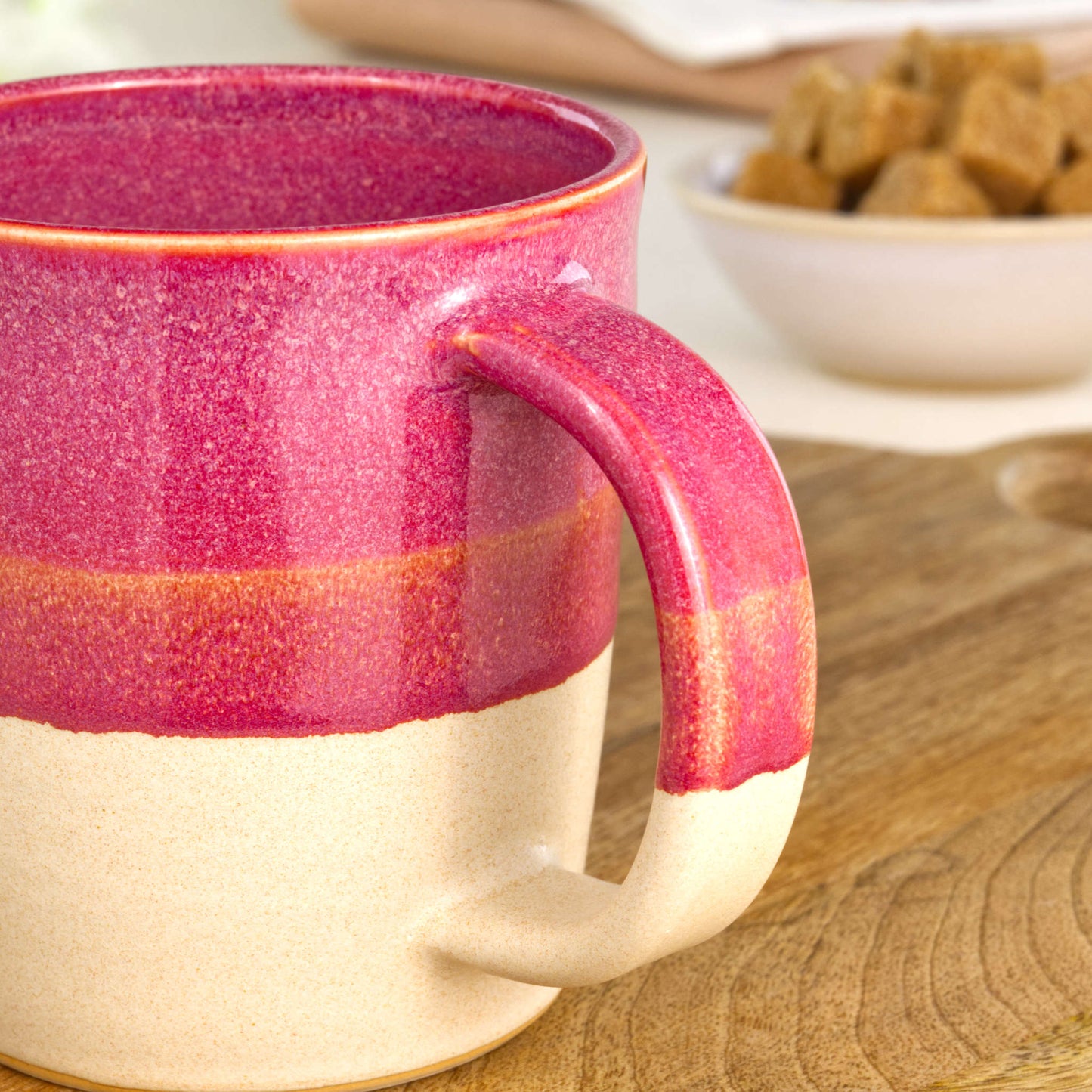Close-up of the handle on a Crimson and Sand handmade coffee mug, finished with glossy Sea Smoothed Pebble glaze above a sandy satin-matte base in my home studio
