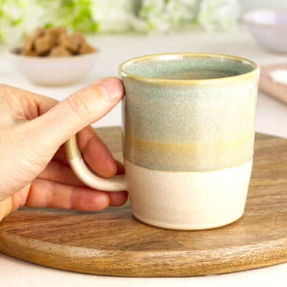 Pale Green and Sand wheel-thrown tea mug shown in hand, highlighting the comfortable handle and tactile feel of this everyday pottery mug from my small UK pottery studio