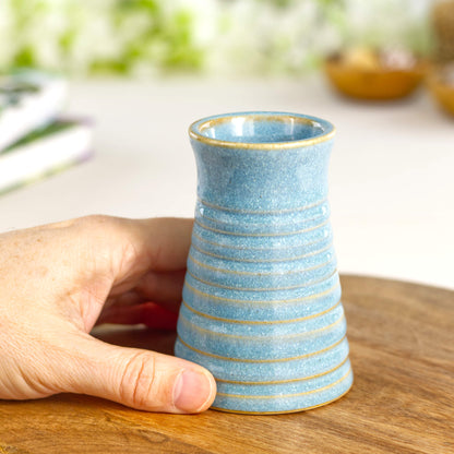 Handmade coastal blue ribbed ceramic bud vase held in hand for scale.