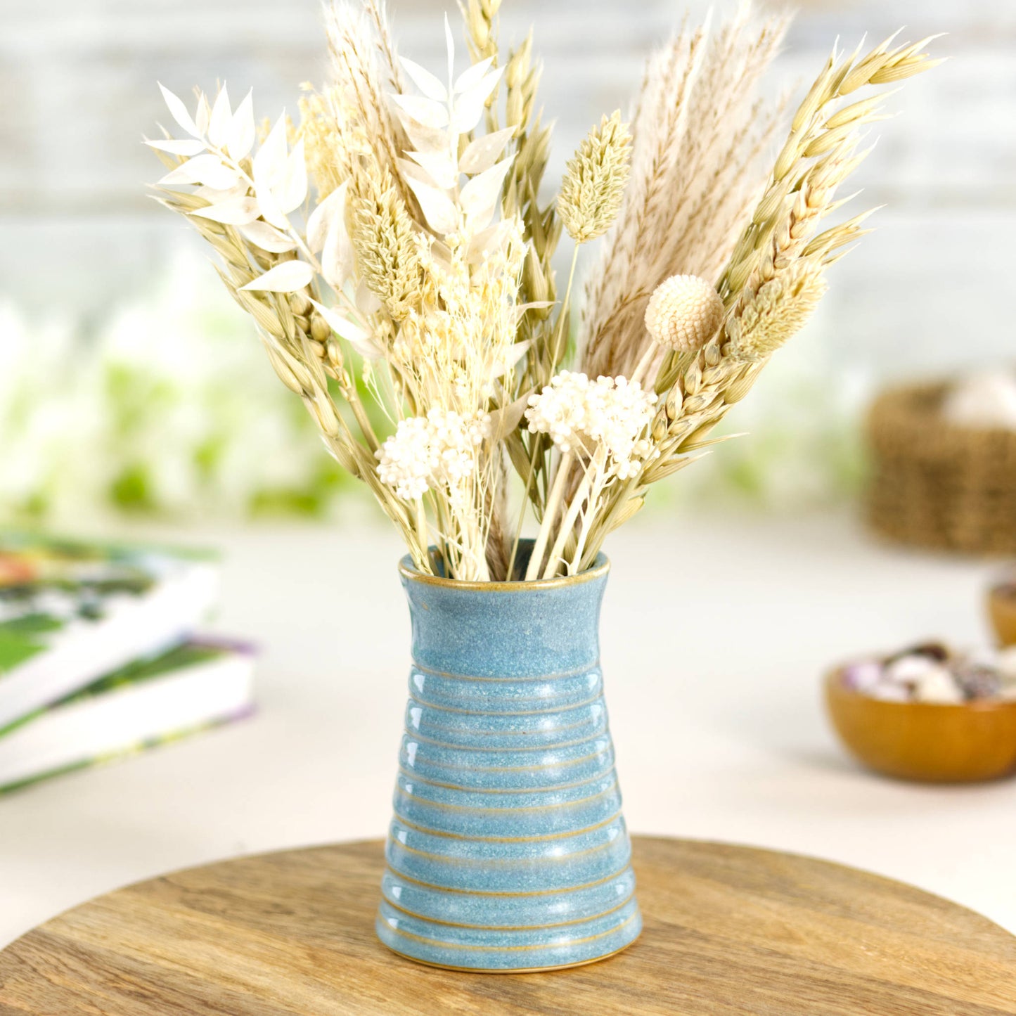 Wheel thrown coastal blue ribbed ceramic bud vase with neutral dried grasses and flowers.