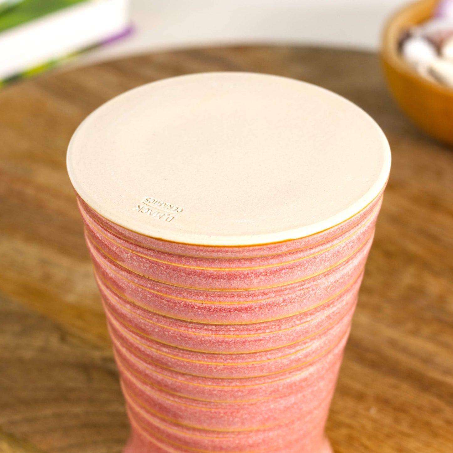 Handmade coral ribbed ceramic bud vase showing the unglazed smooth burnished base with maker’s mark, wheel-thrown studio pottery.