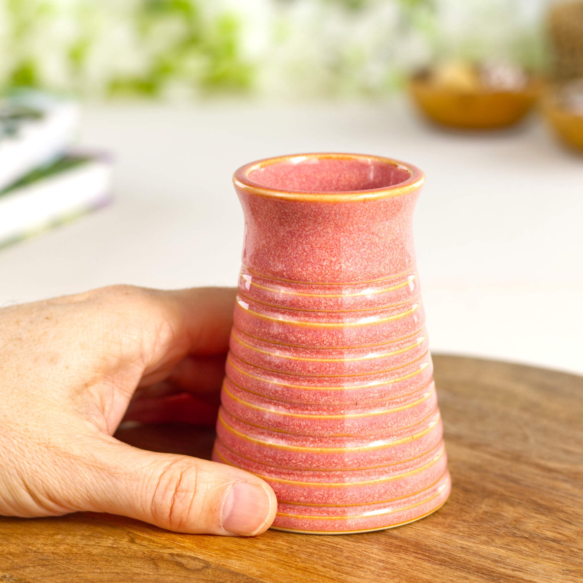 Coral ribbed ceramic bud vase held in hand, showcasing its petite scale and ergonomic form.