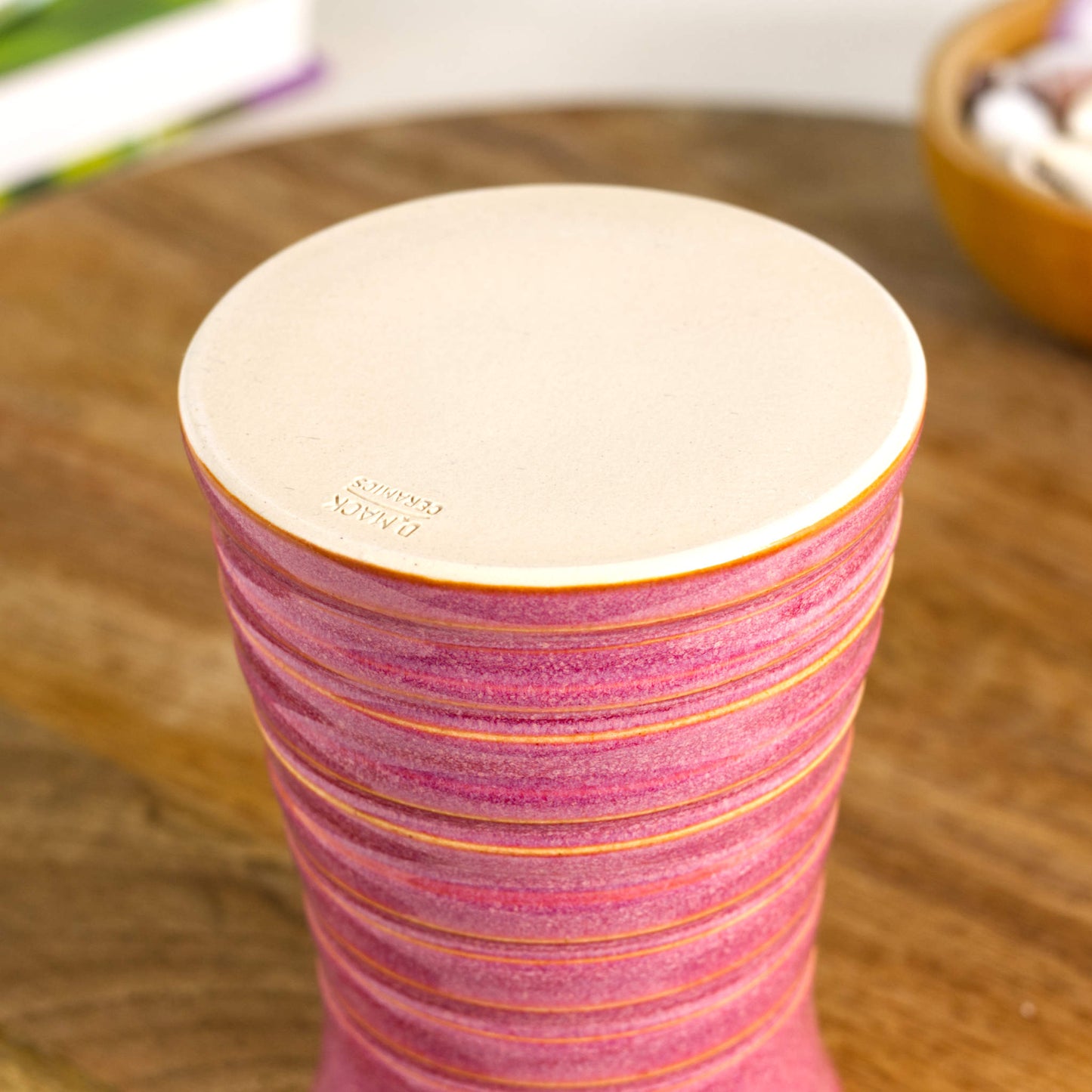 Handmade crimson ribbed ceramic bud vase showing a burnished smooth base with maker’s mark, designed to prevent surface scratching.