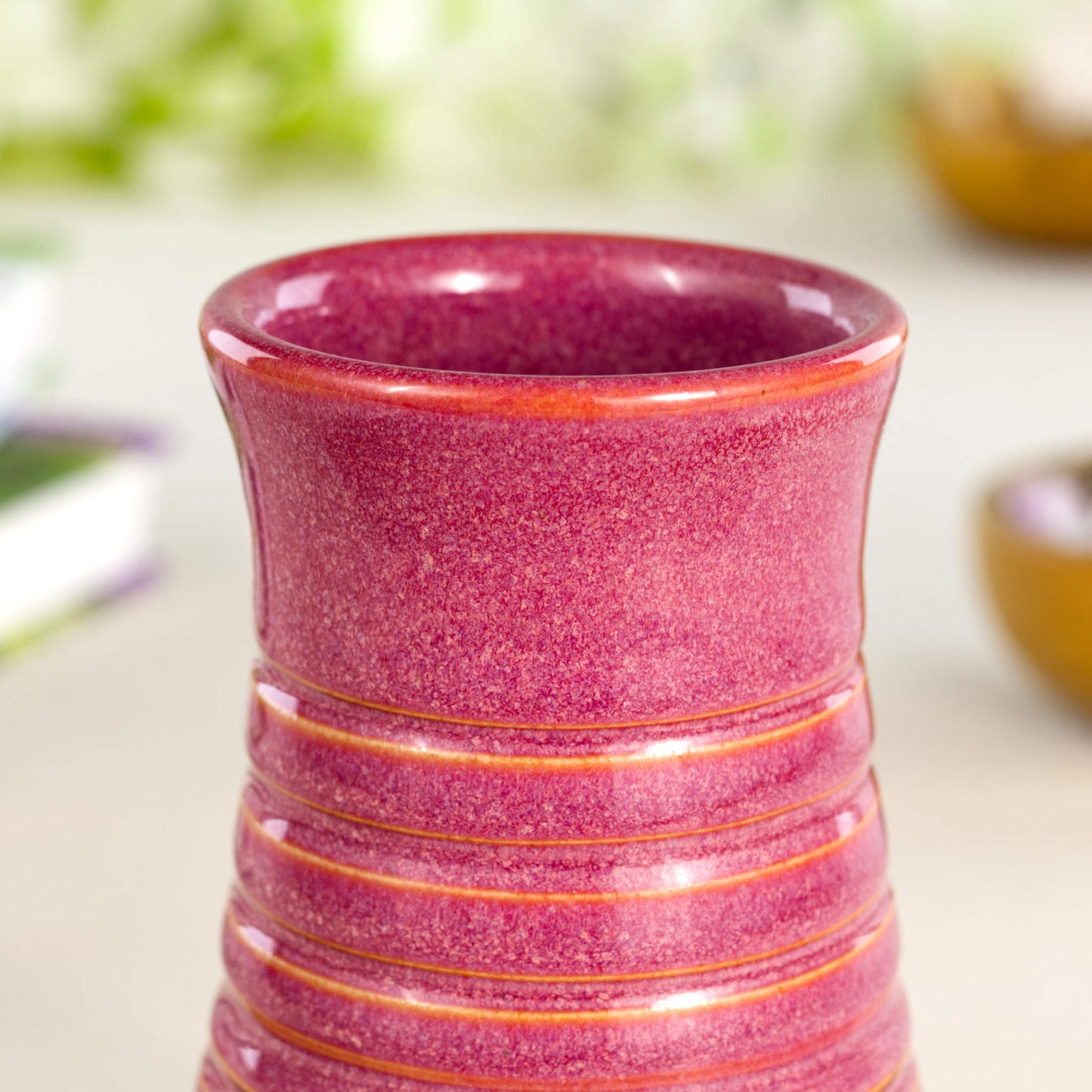Close-up of a crimson glazed ribbed ceramic bud vase highlighting its rich tonal variation and finely textured finish.