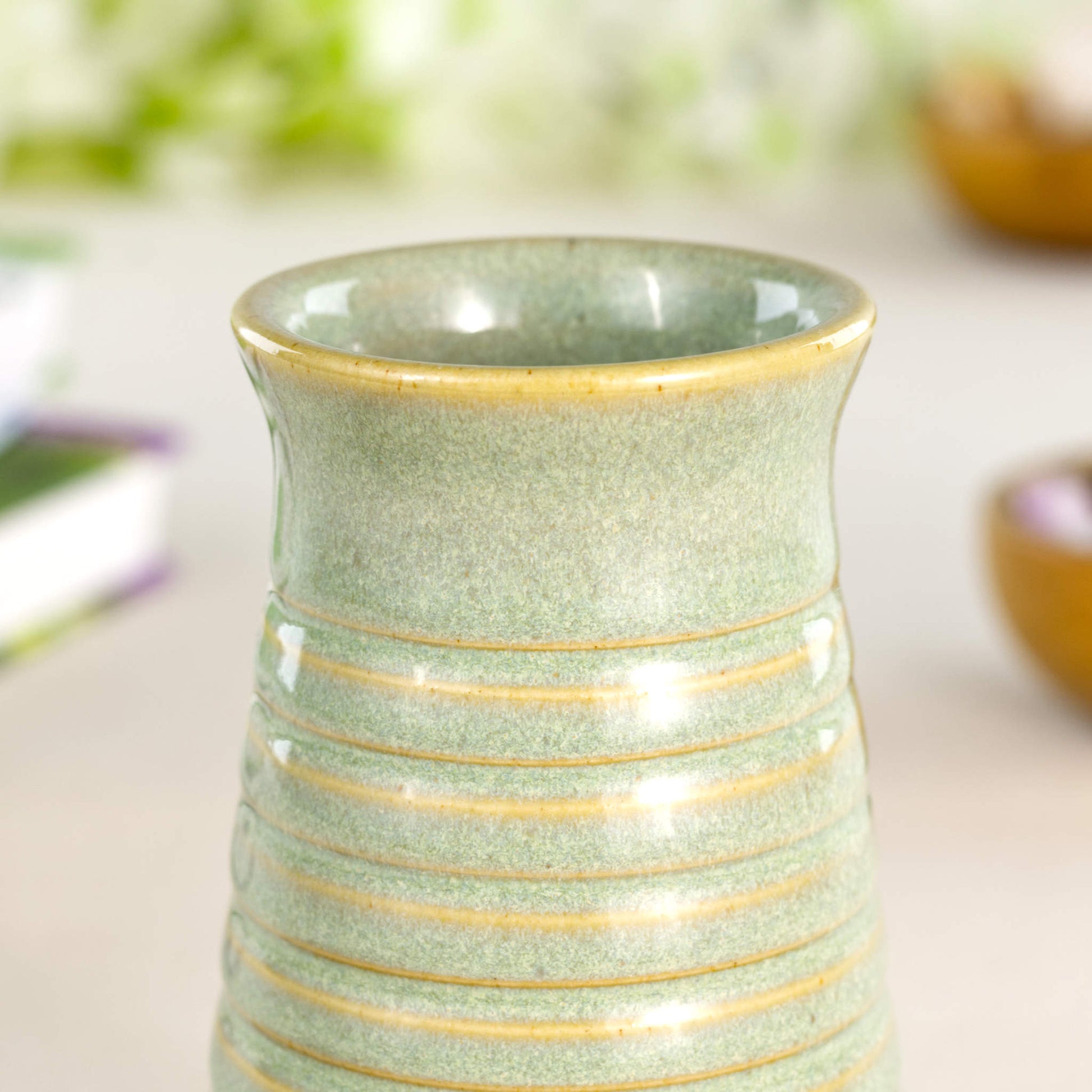 Close-up of a pale green ribbed ceramic bud vase in Sea Smoothed Pebble glaze with a glossy speckled finish.