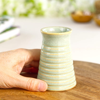 Small handmade pale green ribbed ceramic bud vase held in hand for scale, a wheel-thrown soliflore vase.