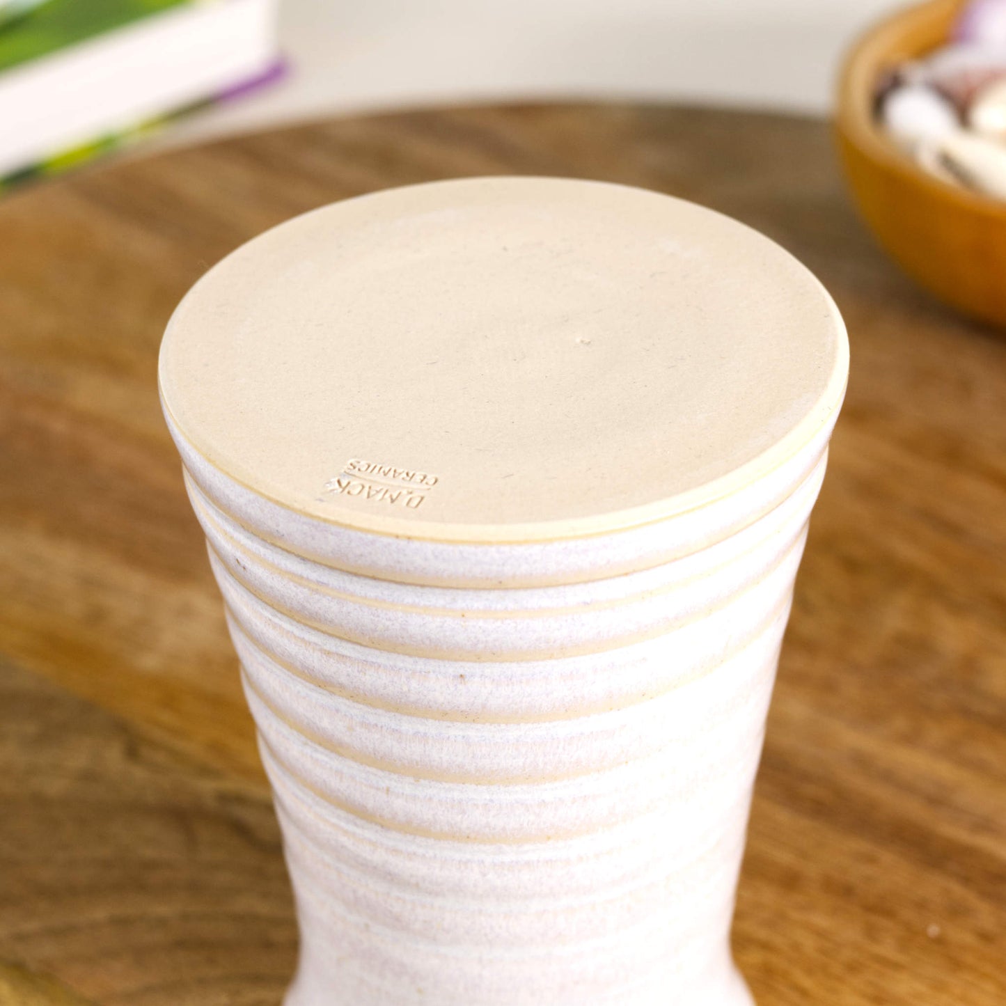Handmade white ribbed ceramic bud vase showing a burnished smooth base with maker’s mark, designed to prevent surface scratching.
