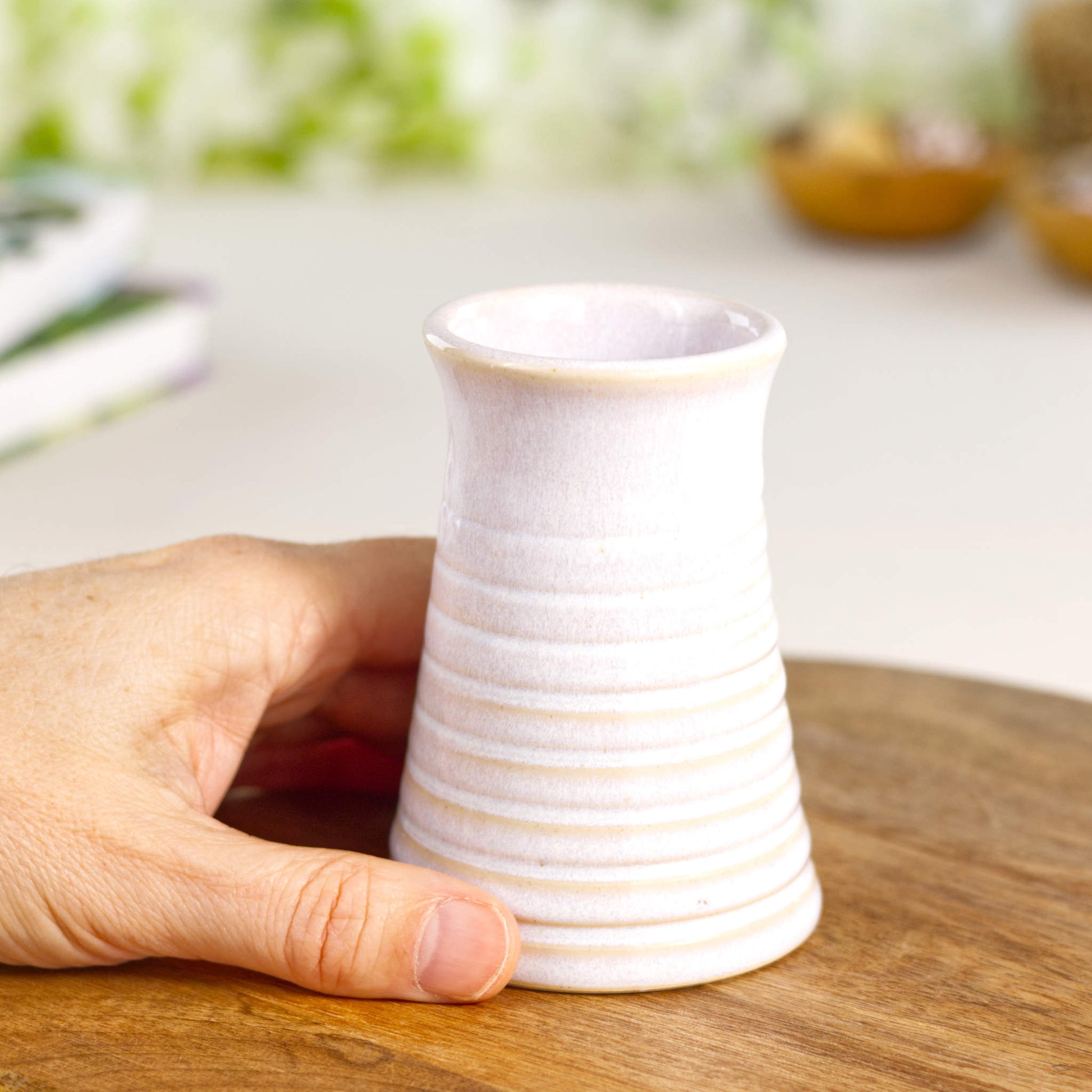 White ribbed ceramic bud vase held in hand, highlighting its delicate scale and minimalist handcrafted form.
