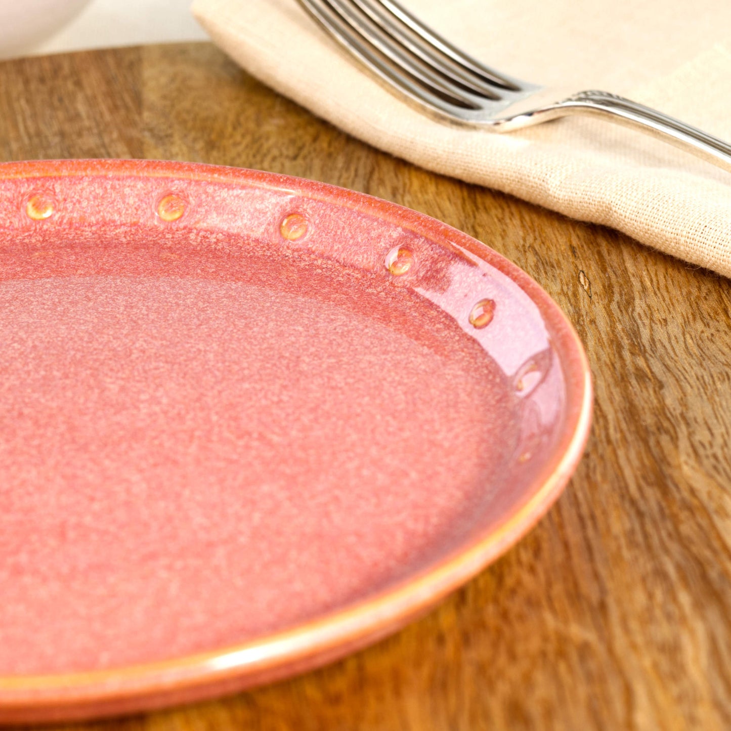 Close-up of a Coral ceramic small plate, highlighting the glossy speckled glaze, hand-finished dotted rim and warm peachy stoneware tones