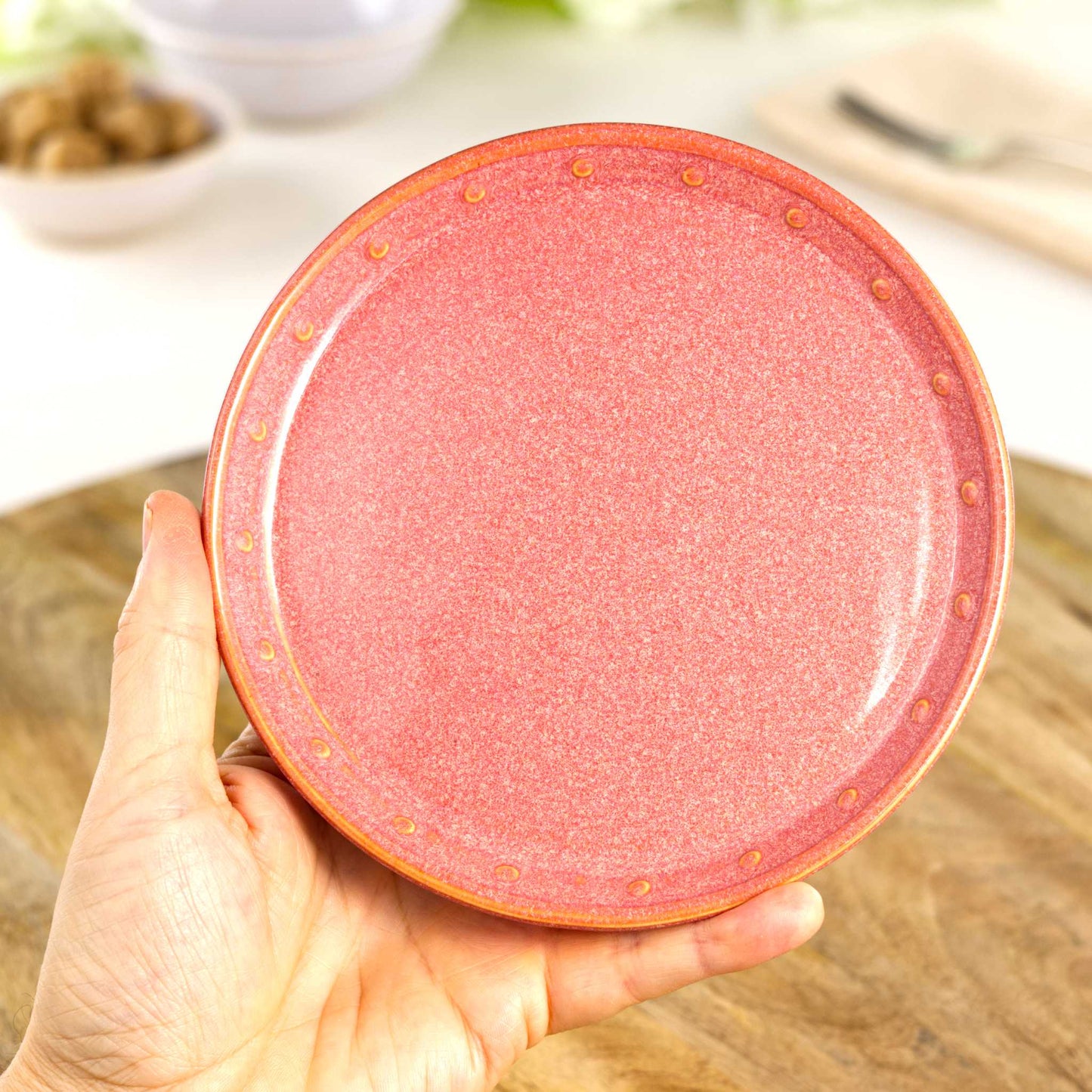 Handmade Coral small plate held in the hand, a wheel-thrown stoneware side plate from a small British artisan studio