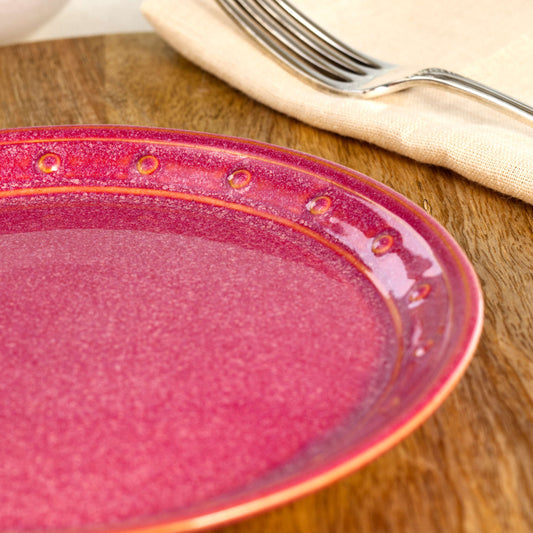 Close-up of a Crimson ceramic small plate, highlighting the glossy speckled glaze, hand-finished dotted rim and rich red stoneware finish