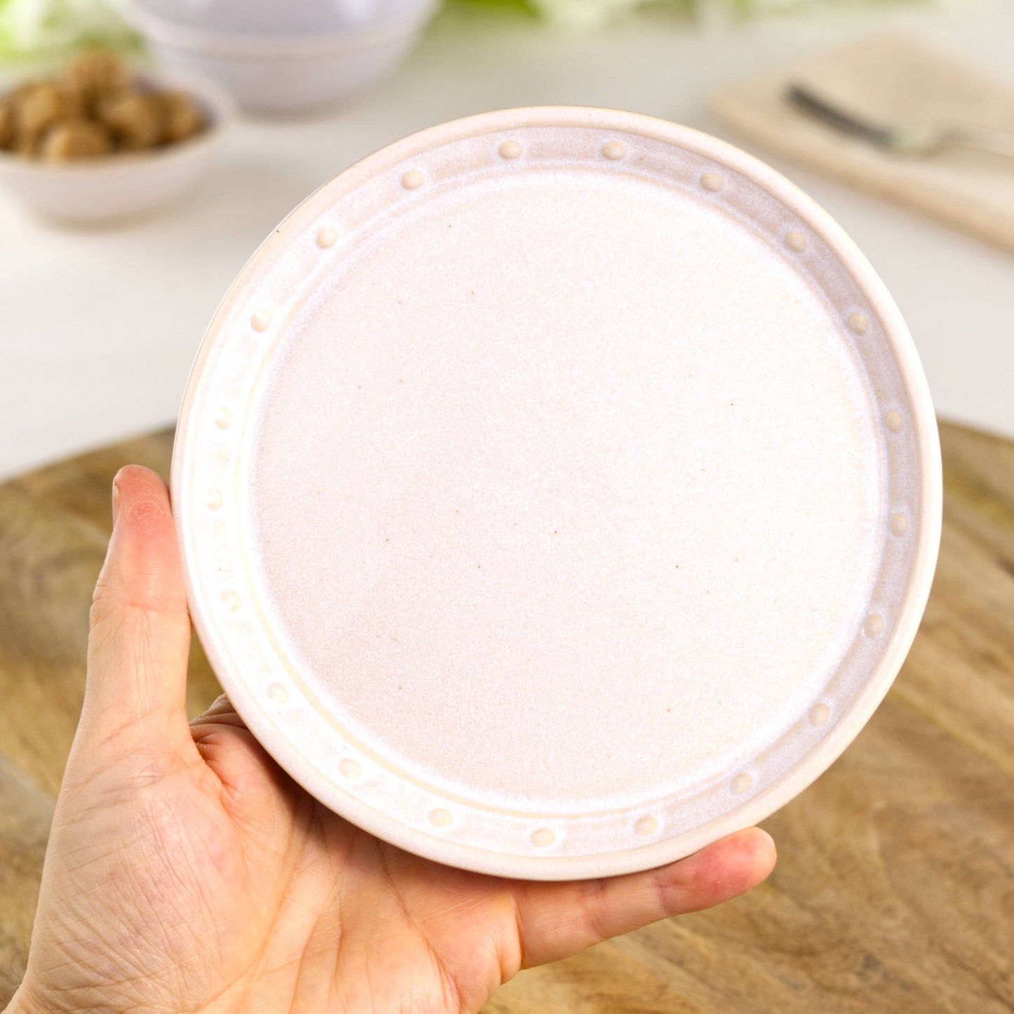 Handmade white ceramic small plate held in the hand, a wheel-thrown stoneware side plate from a small British artisan studio