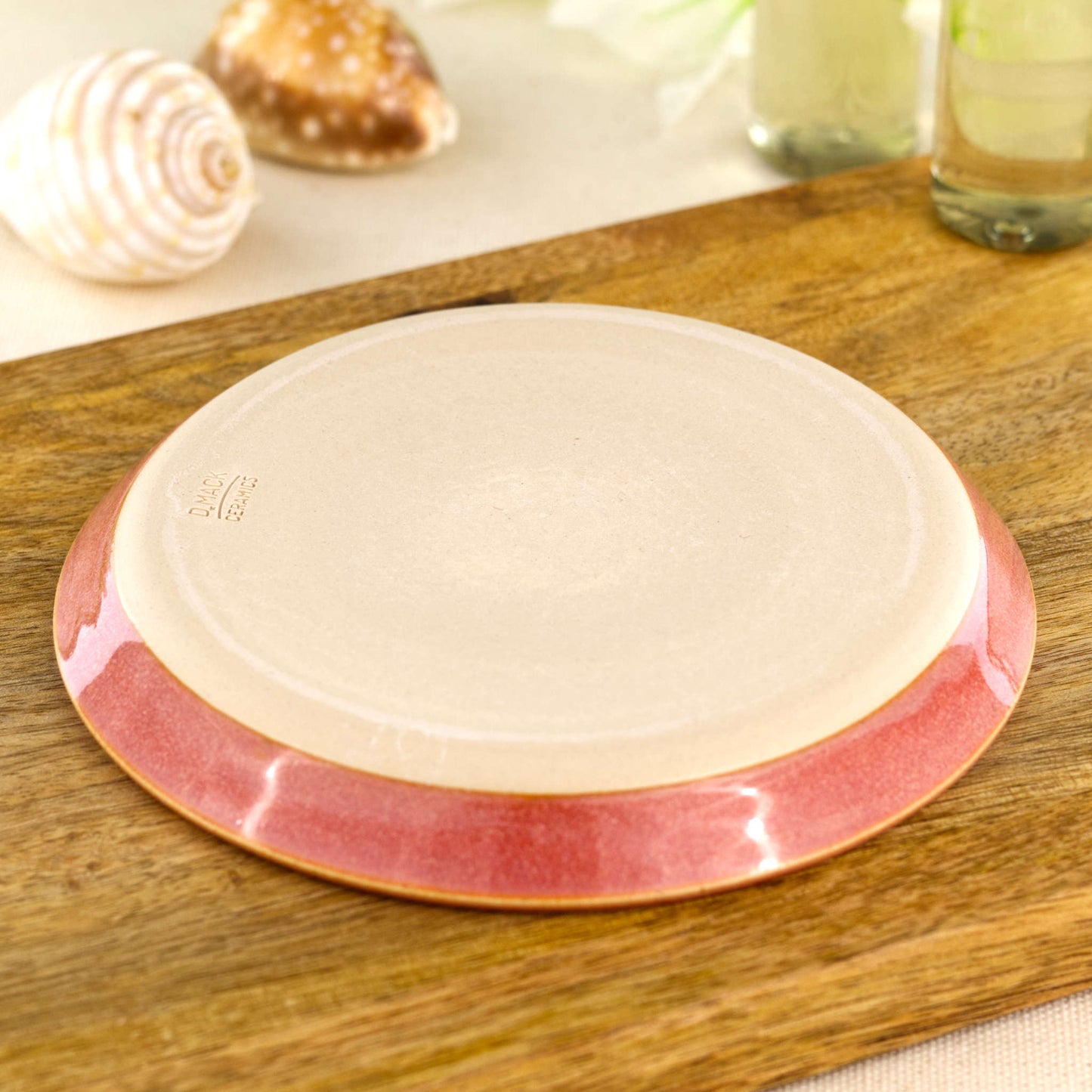 Base of handmade coral pottery soap dish showing smooth burnished underside and impressed makers mark, wheel-thrown ceramic soap holder for sink area