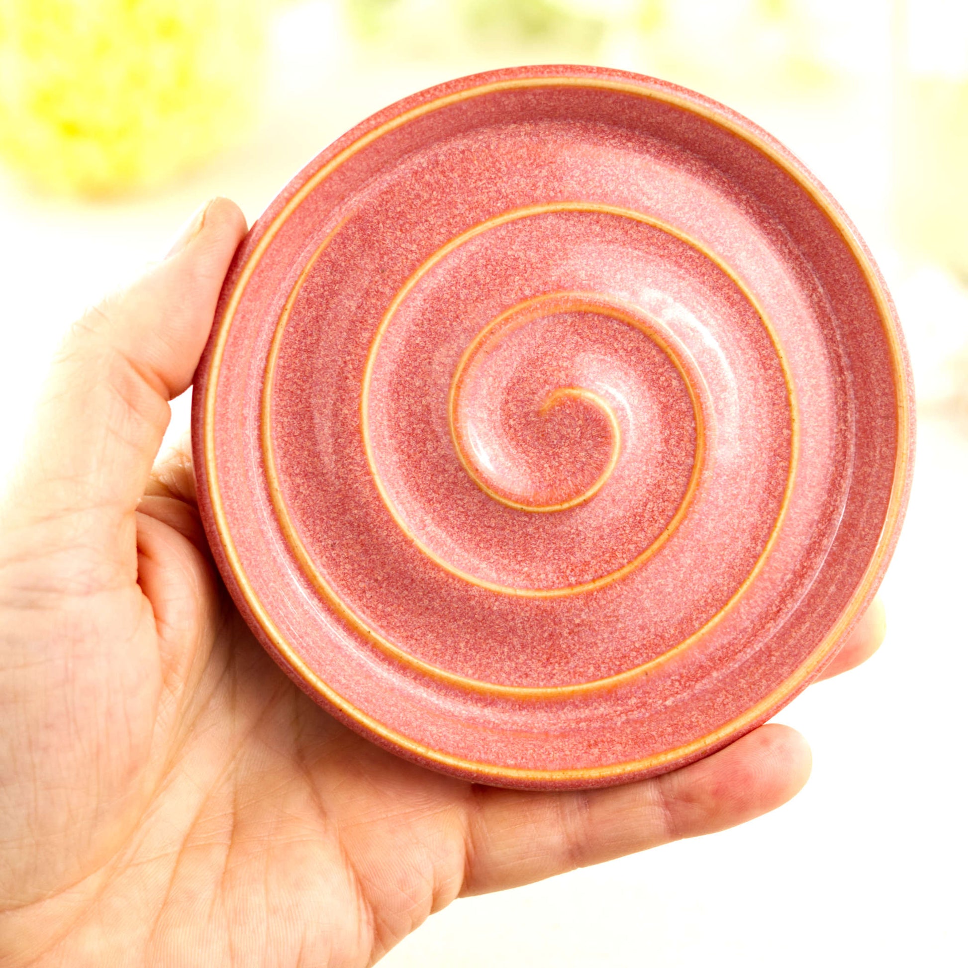 Coral handmade pottery soap dish held in hand showing size, artisan ceramic soap saver with raised spiral drainage design