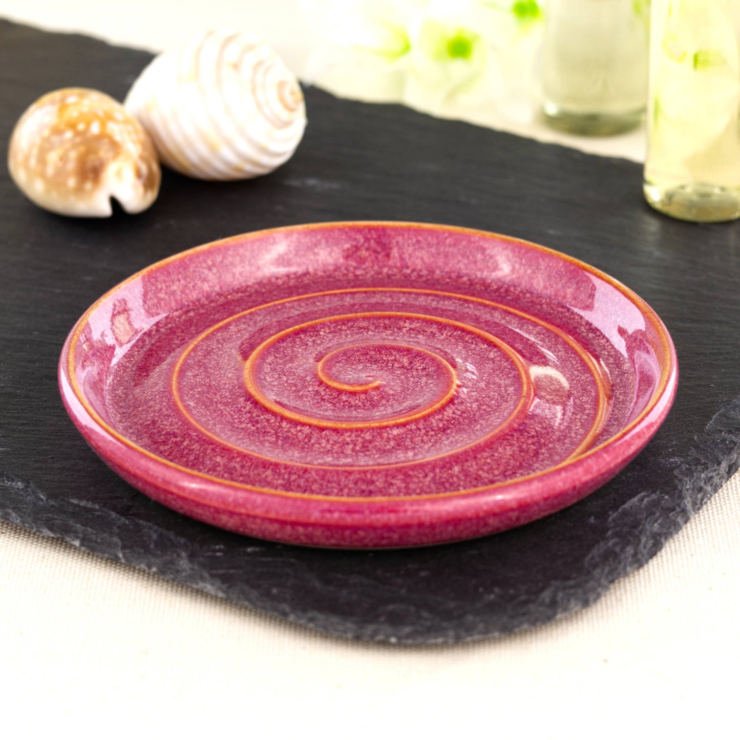 Handmade crimson ceramic soap dish with spiral ridges, wheel-thrown stoneware bathroom accessory on black slate with coastal shell styling