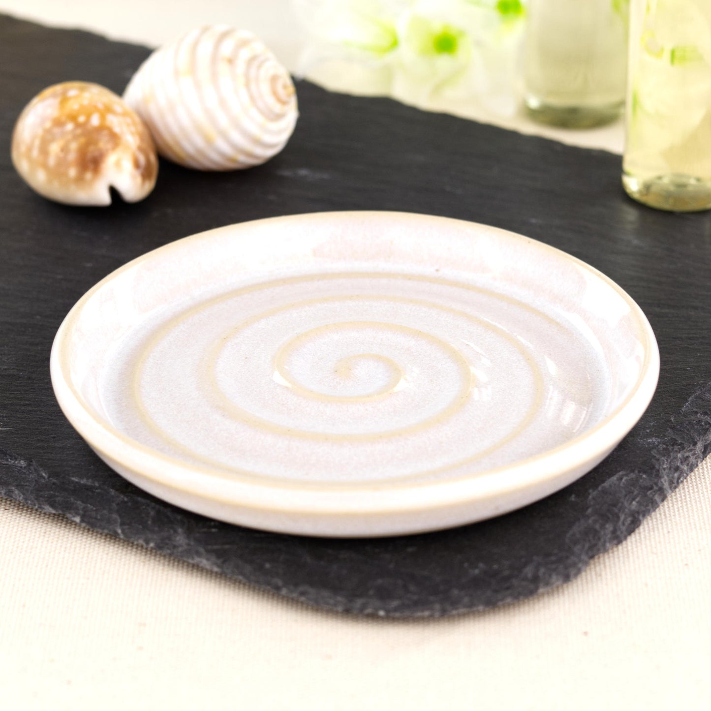 Handmade white ceramic soap dish with spiral ridges, wheel-thrown stoneware bathroom accessory on black slate with coastal shell styling