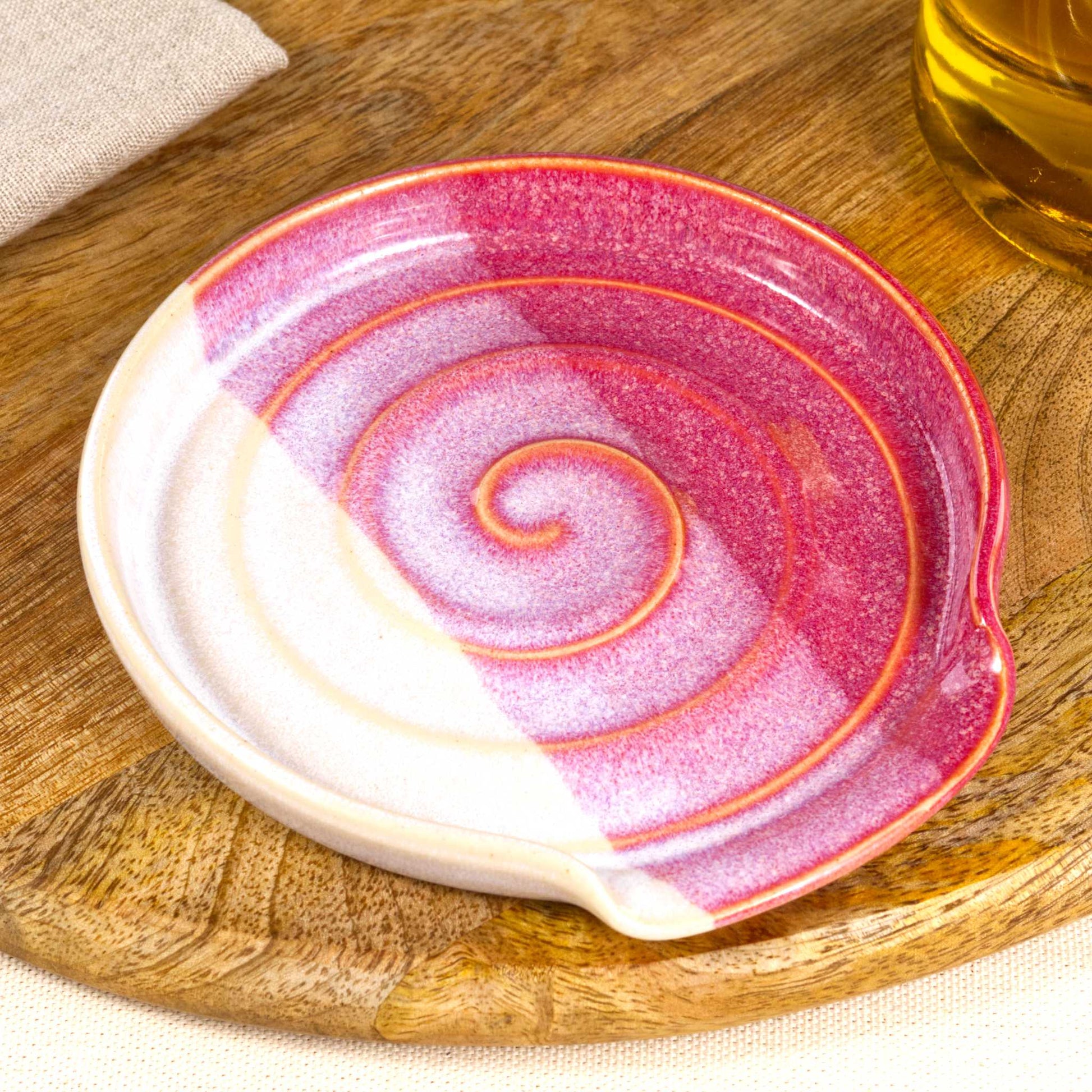 Close up of crimson and white pottery spoon rest with glossy speckled glaze, handmade ceramic utensil rest with spiral detail