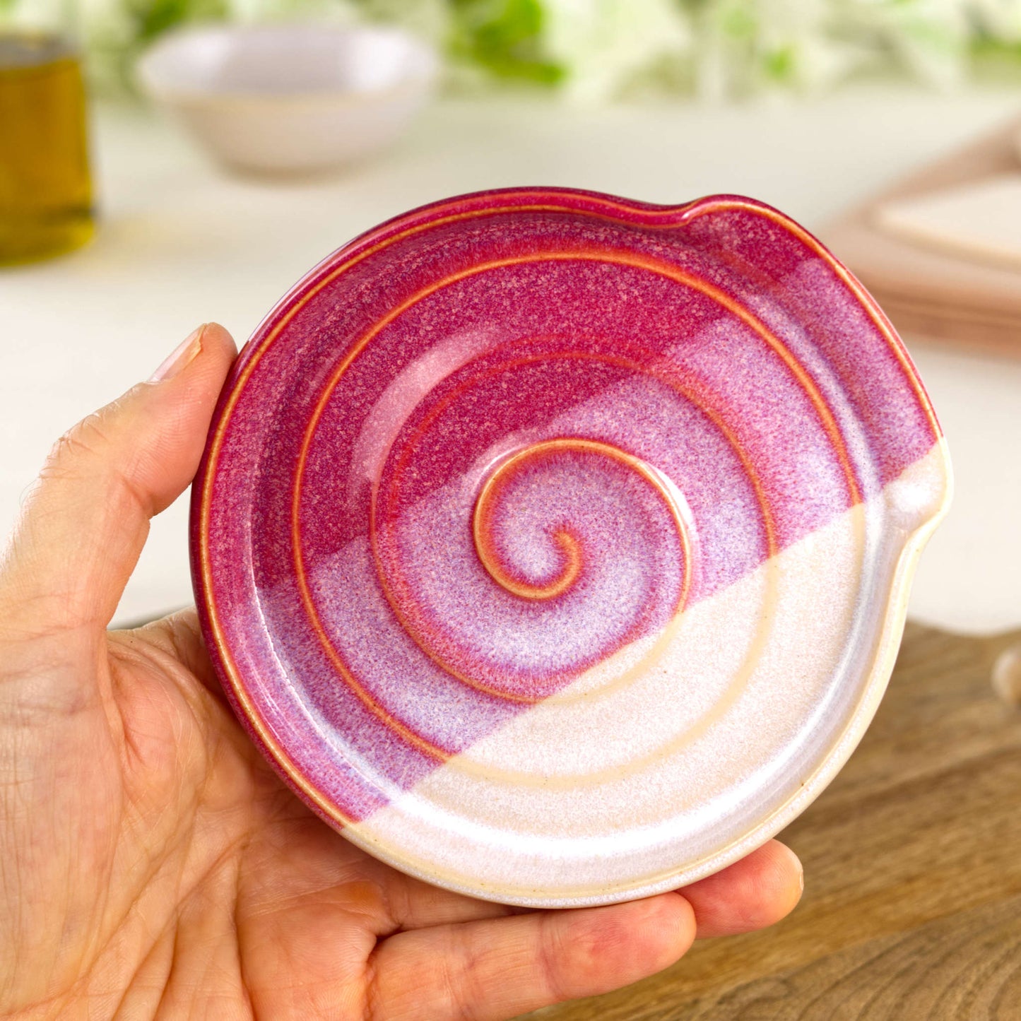 Handmade crimson and white ceramic spoon rest shown in hand, compact wheel-thrown stoneware spoon holder for kitchen worktop