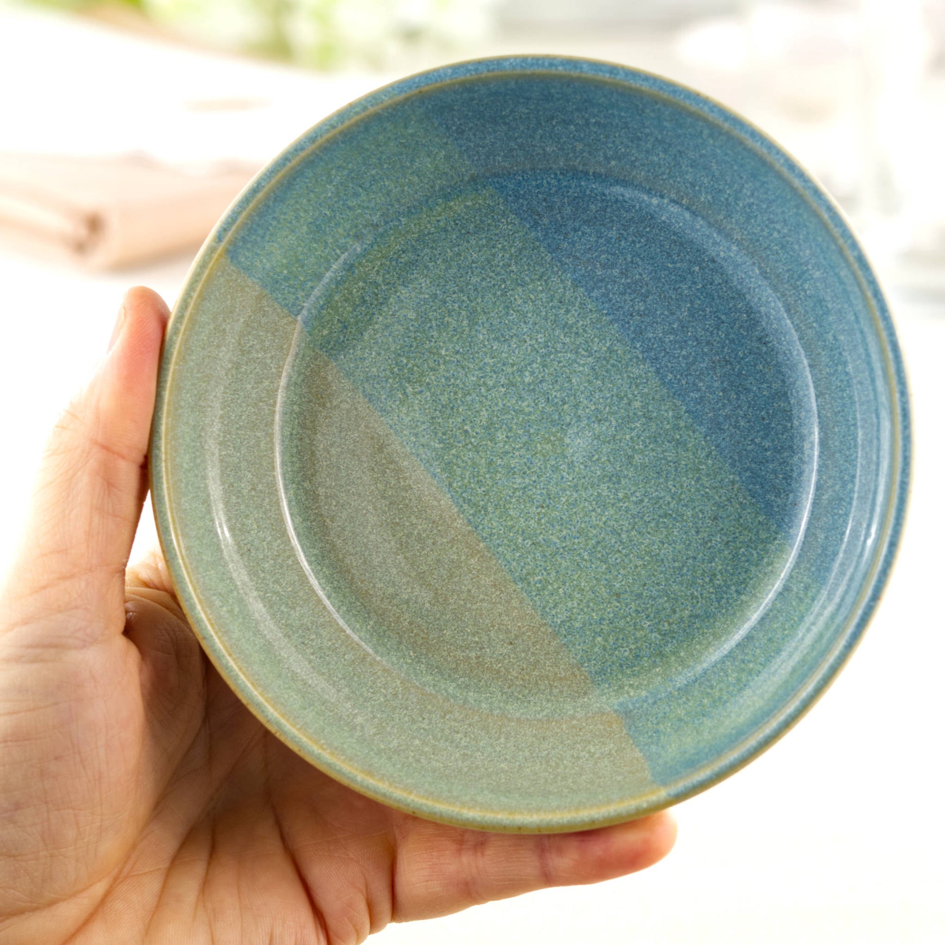 Handmade ceramic tapas bowl held in the hand, finished in Coastal Blue & Pale Green glazes with a flatter interior designed for tapas-style serving, side dishes and sharing food